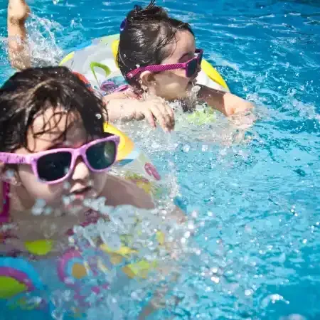 Two children wearing sunglasses in a pool, splashing water.