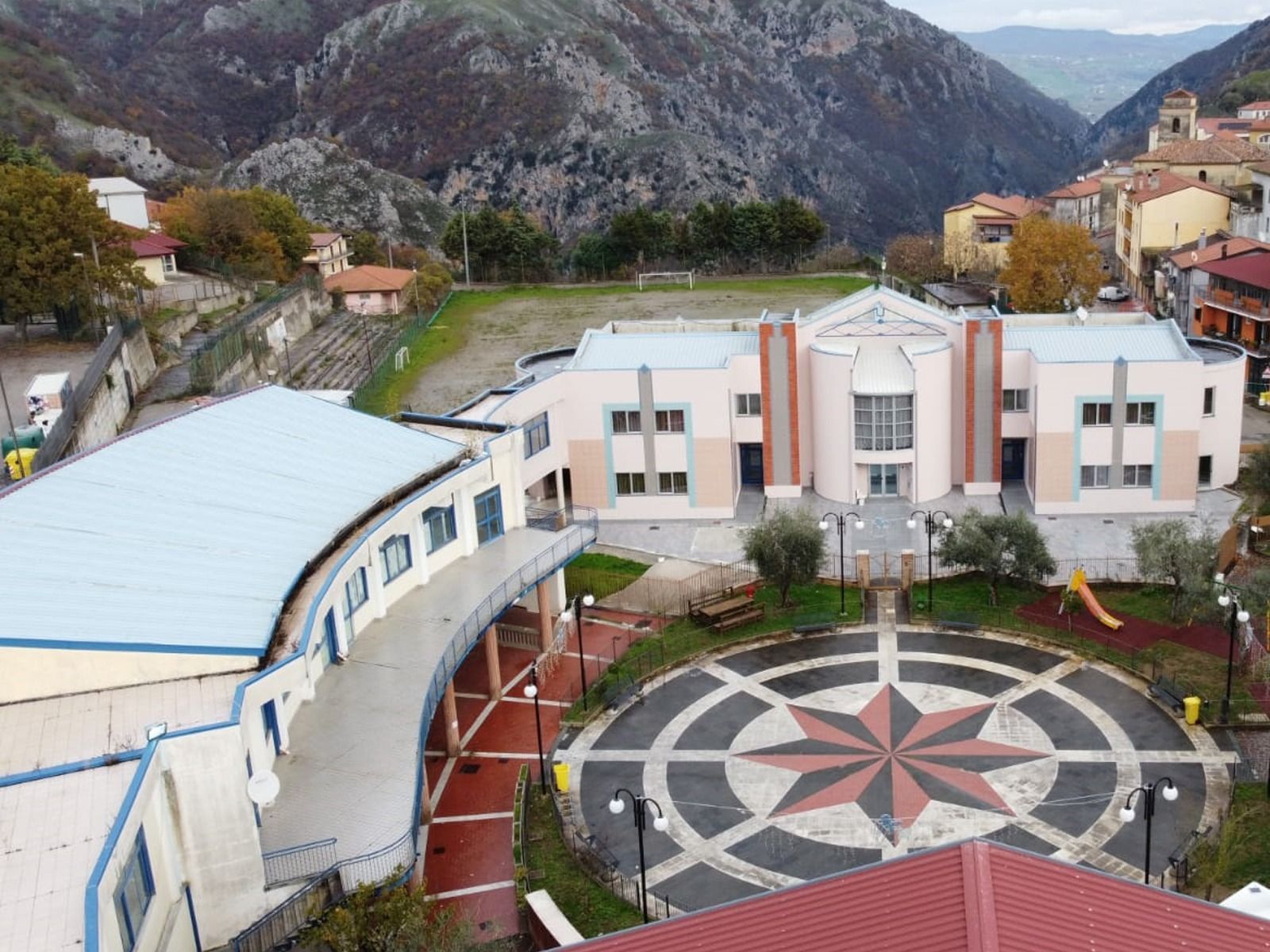 Una piazza cittadina con un edificio di fronte alle montagne. La piazza ha una pianta a forma di compasso.