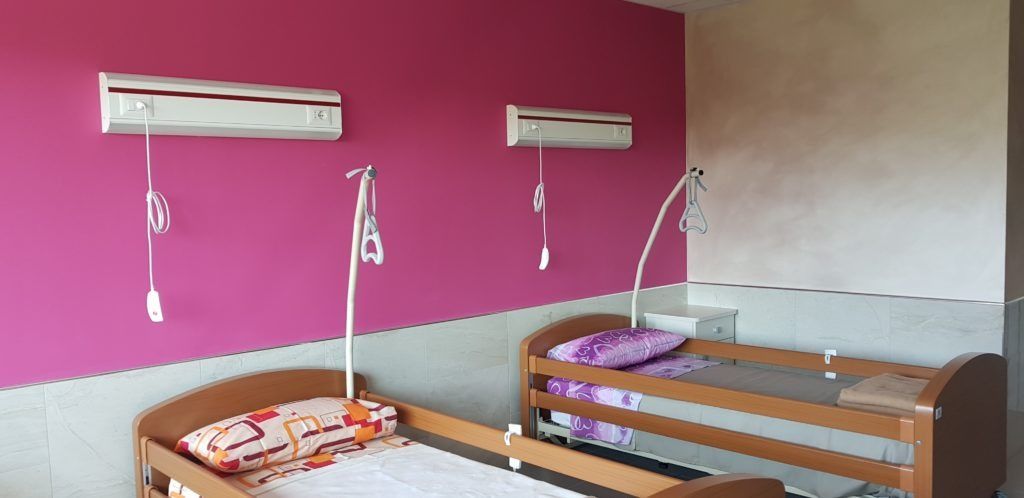 Due letti in una stanza con pareti rosa e beige. Ogni letto ha un supporto sopraelevato ed è appoggiato a una parete.