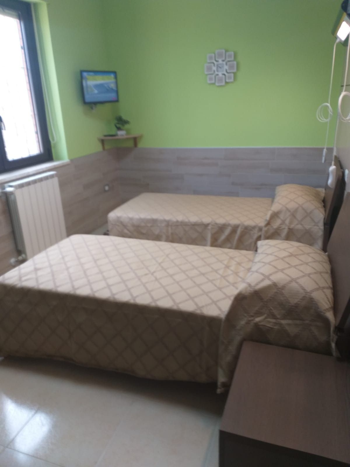 Una piccola stanza con due letti, pareti verdi, una piccola TV e un orologio decorativo.
