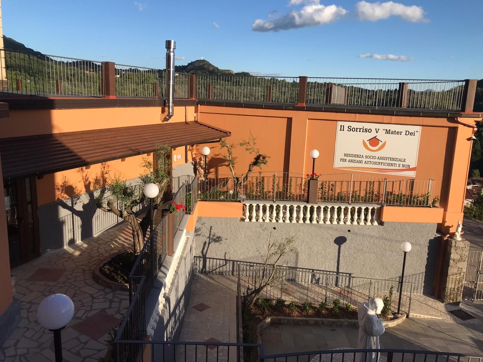 Vista esterna di un ristorante con pareti arancioni e un'insegna. Area terrazzata, montagne sullo sfondo.