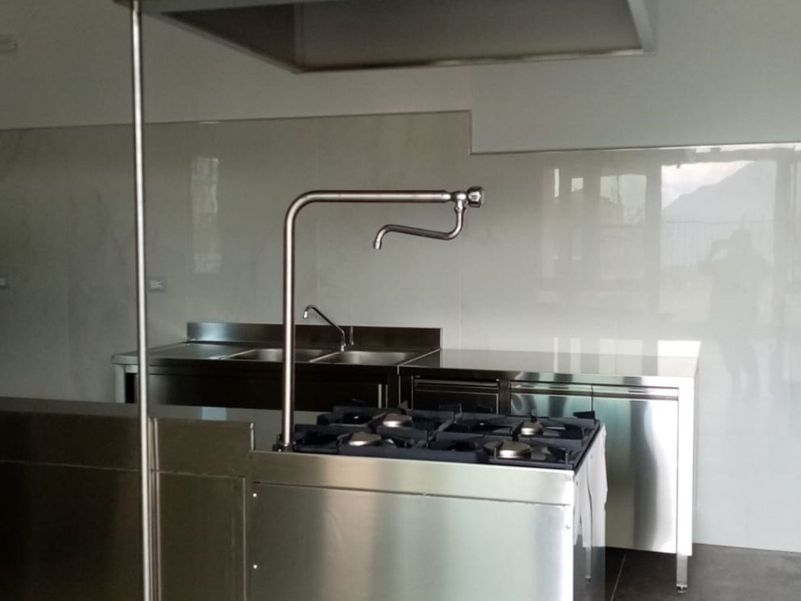 Cucina commerciale in acciaio inox con piano cottura, rubinetto e lavelli.