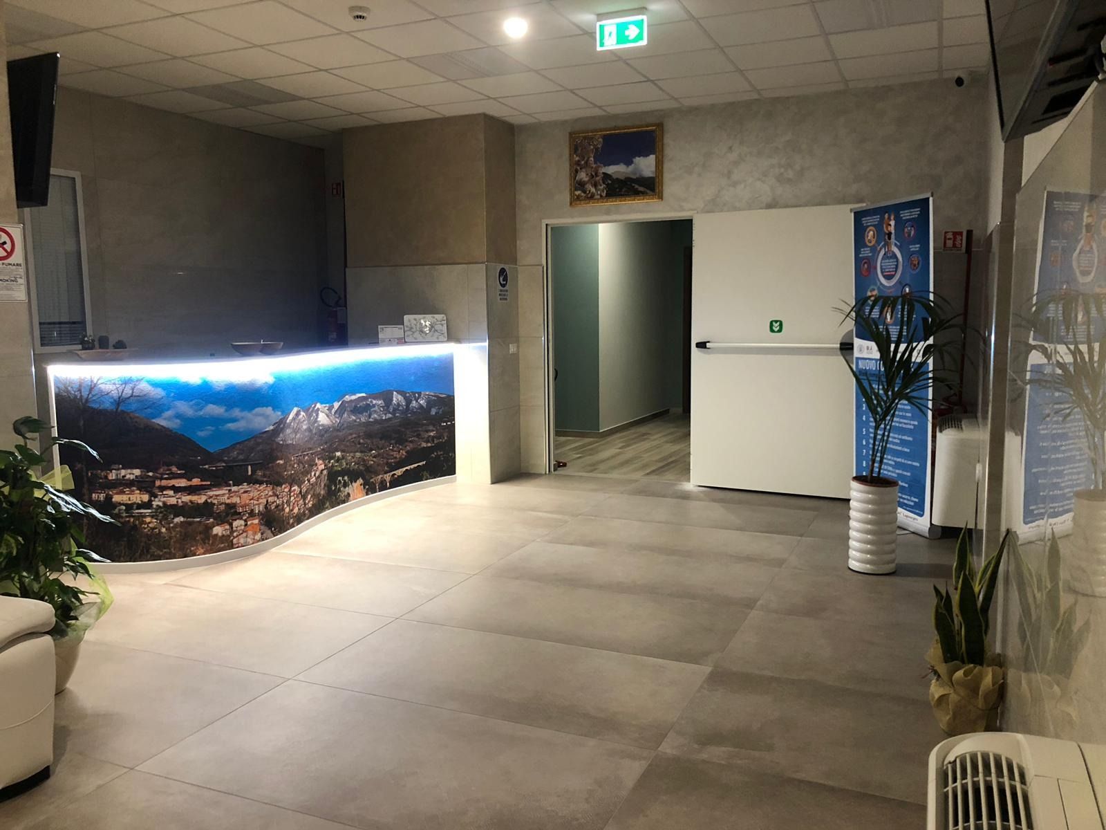 Hall con bancone curvo raffigurante una scena di montagna, porta aperta, piante e pavimento piastrellato.