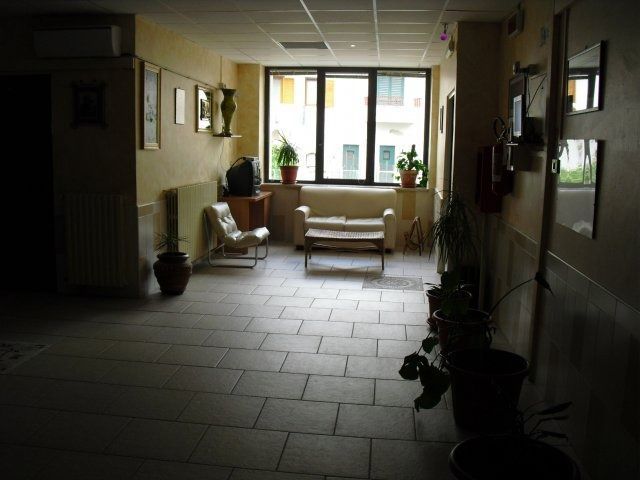 Corridoio con pavimento piastrellato, zona salotto vicino alla finestra, piante e opere d'arte.