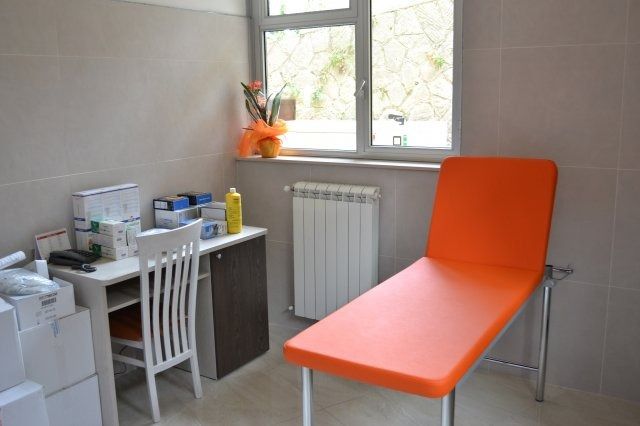 Sala visite con tavolo arancione, scrivania e finestra.