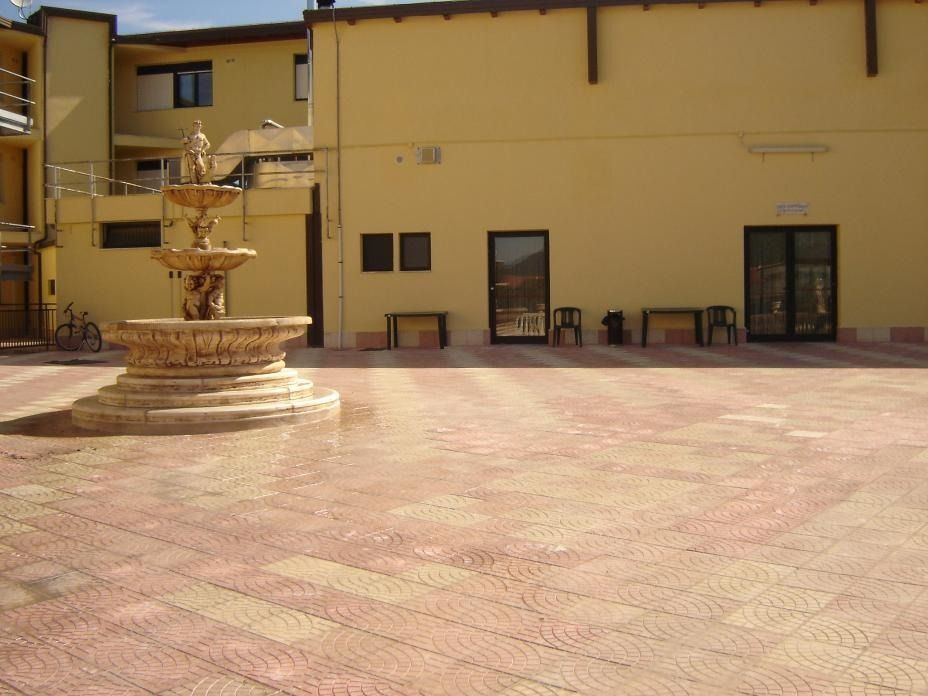 Fontana in un cortile lastricato di mattoni con edifici gialli sullo sfondo.