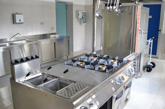 Cucina commerciale con elettrodomestici in acciaio inossidabile, tra cui piano cottura, friggitrice e lavelli.