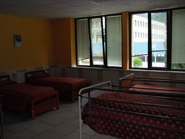 Una stanza con quattro letti, una finestra con le persiane e le pareti gialle.