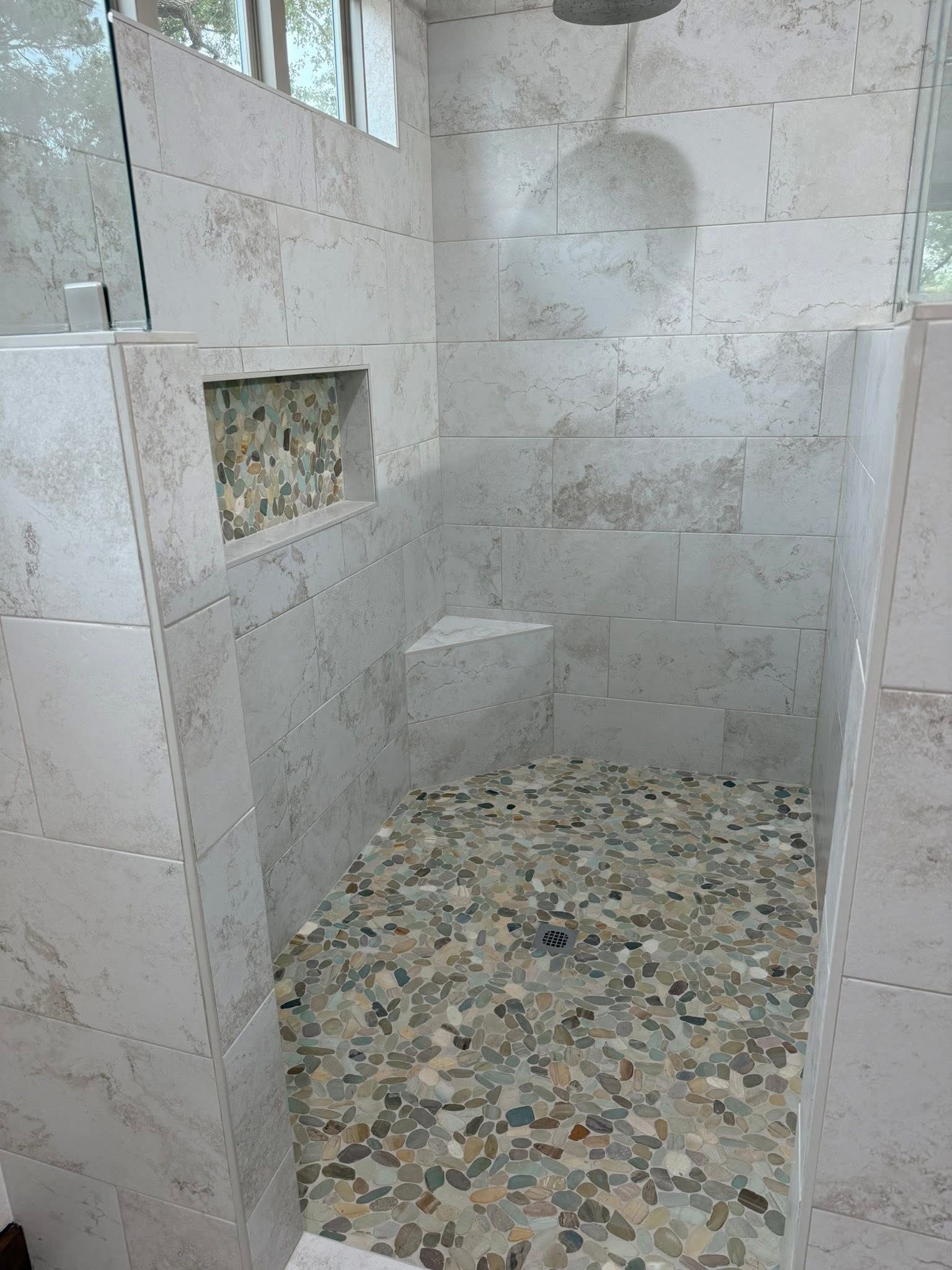 Modern bathroom with patterned tile walls, freestanding tub, and pebble shower floor.