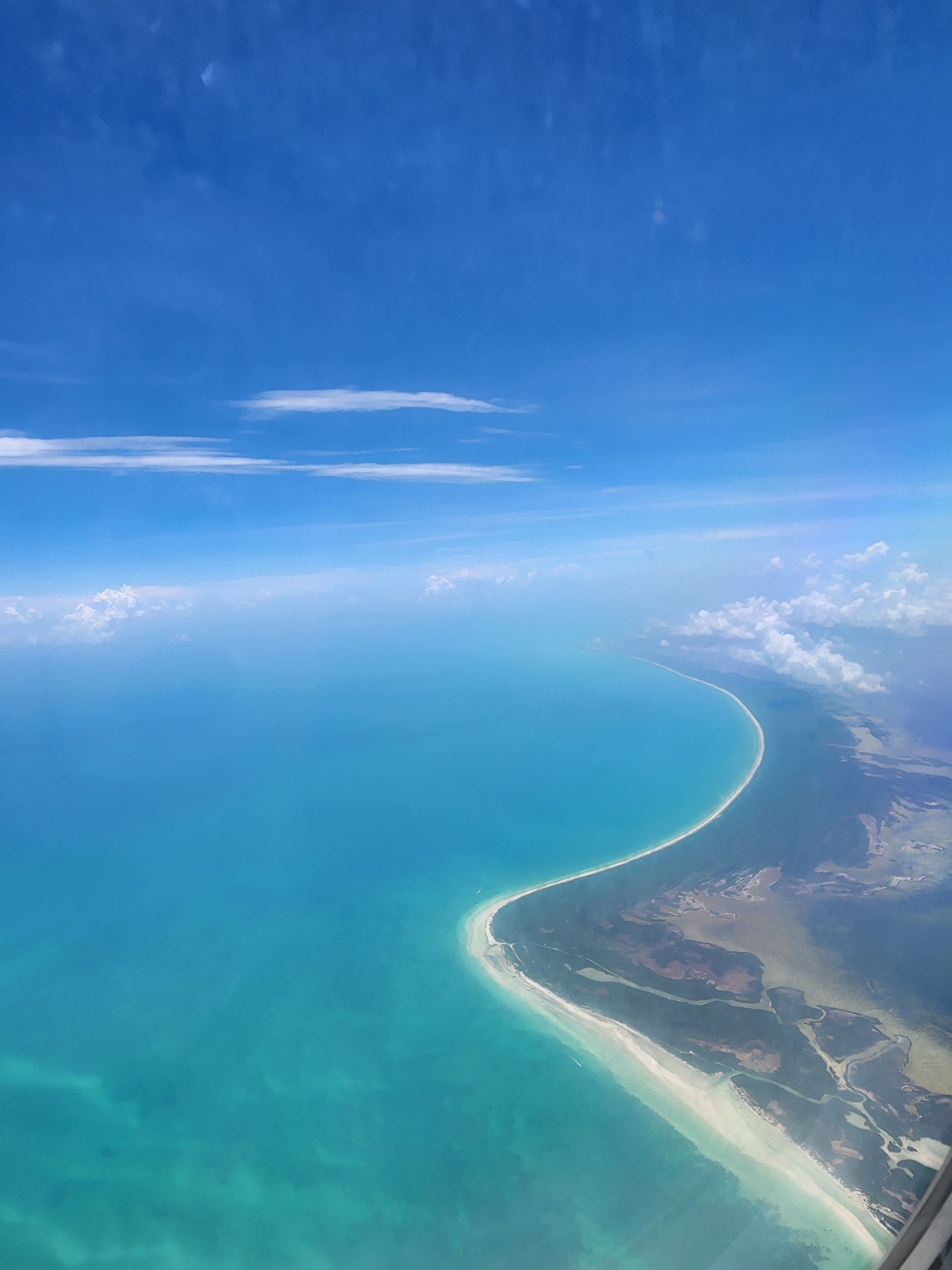 Aerial view of a curved, sandy beach meeting turquoise ocean waters under a clear blue sky.