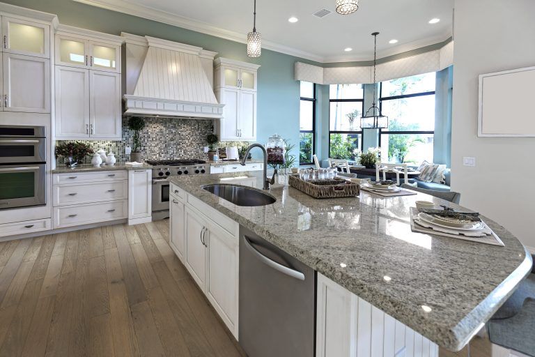 A kitchen with white cabinets , granite counter tops , stainless steel appliances and hardwood floors.