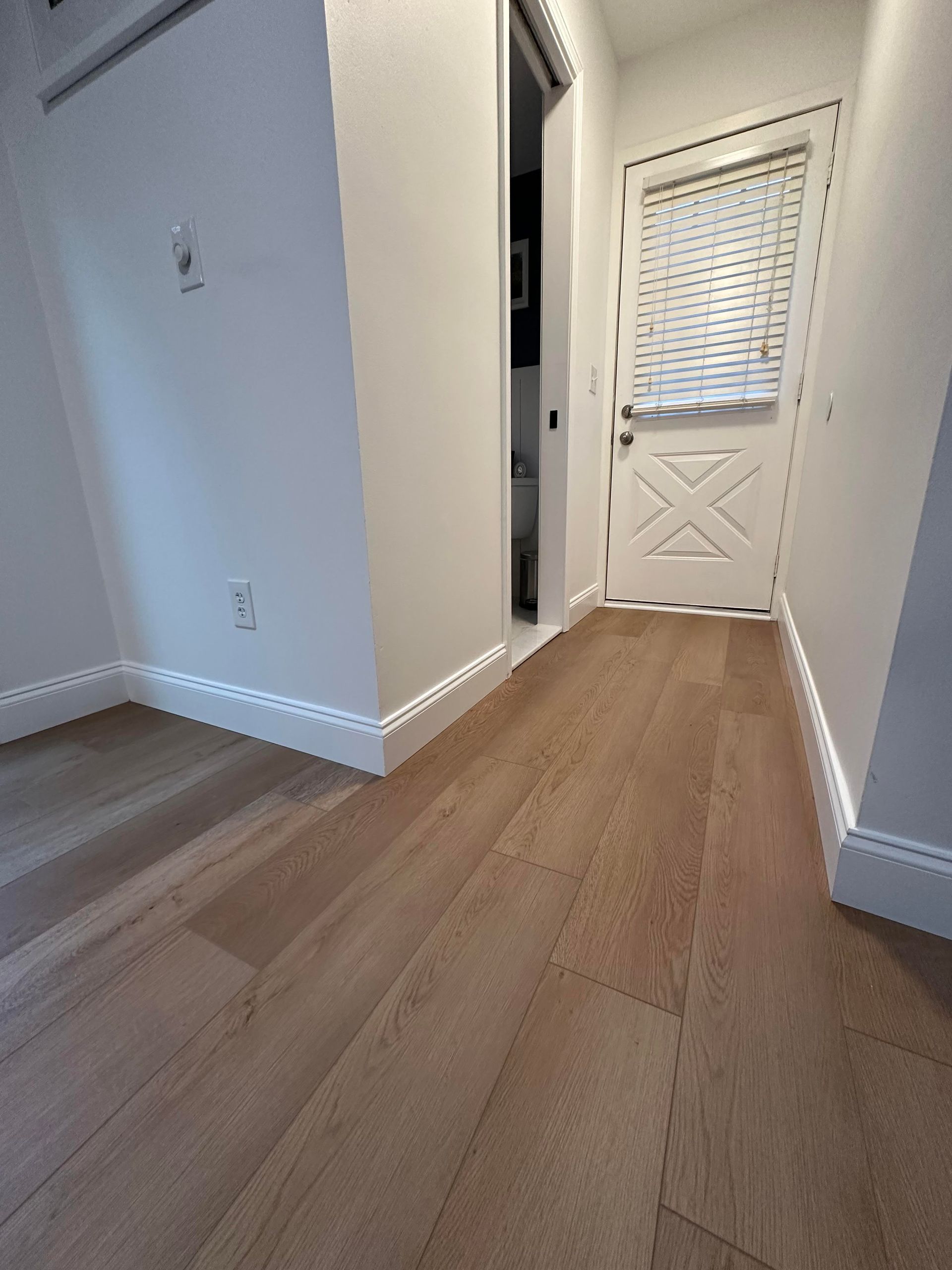 A hallway with hardwood floors and white walls leading to a door.