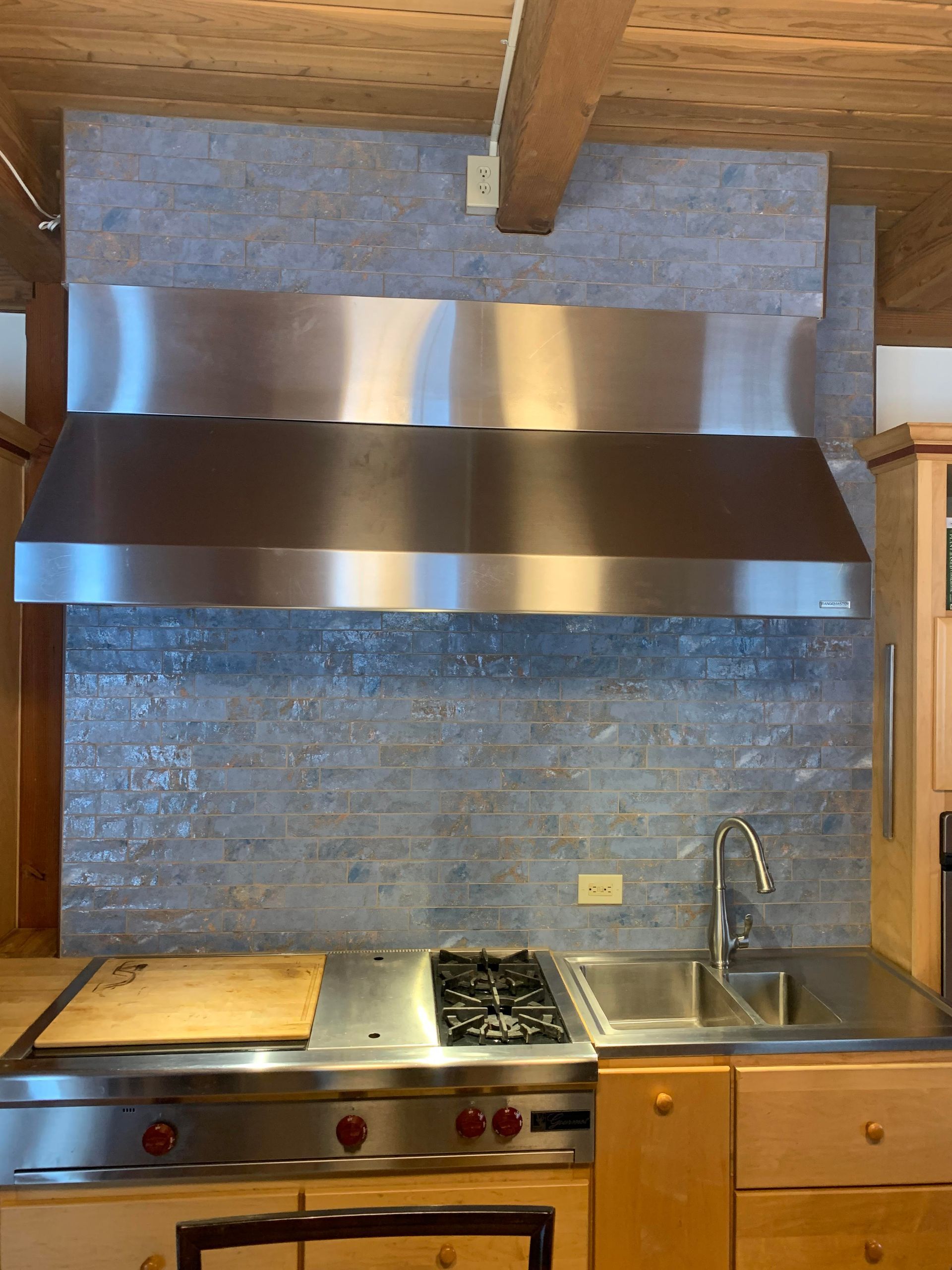 A kitchen with a stove , sink , and stainless steel hood.