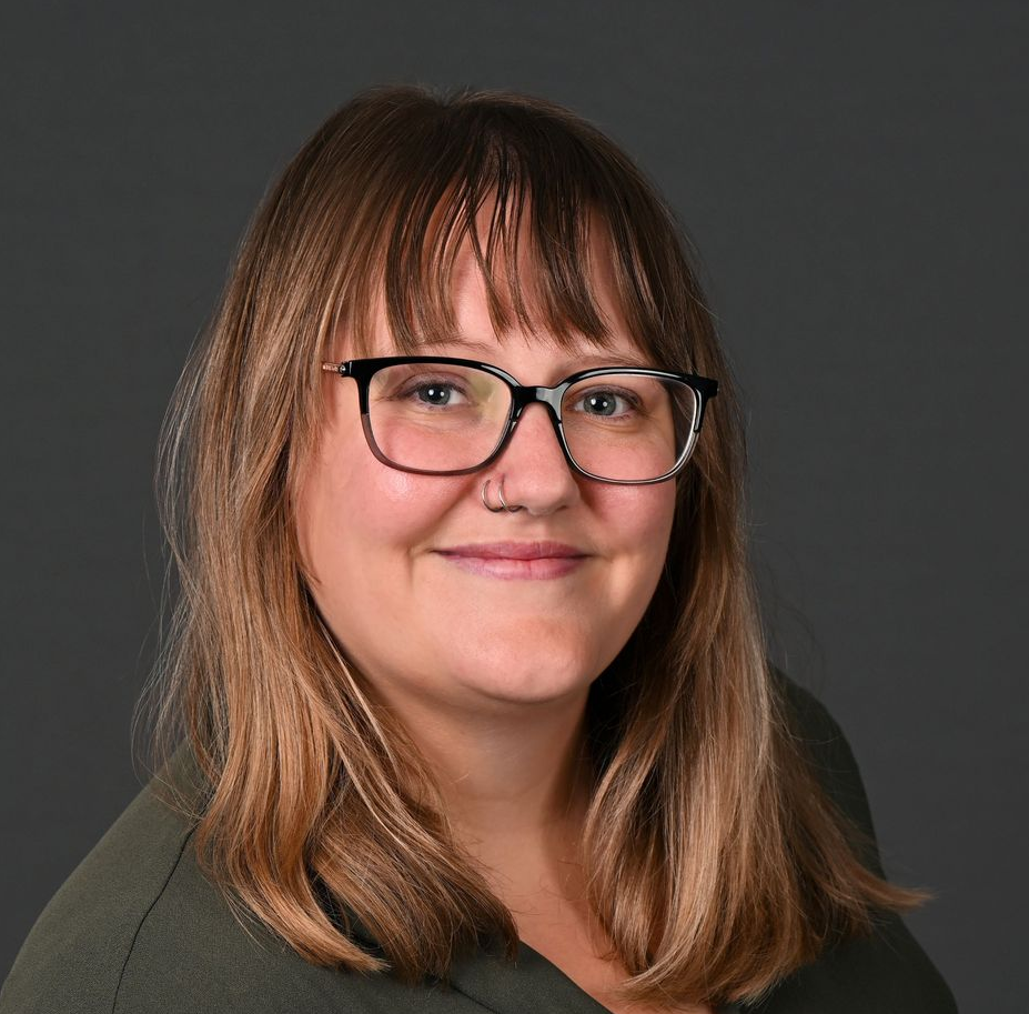 A woman wearing glasses and earrings is smiling for the camera.