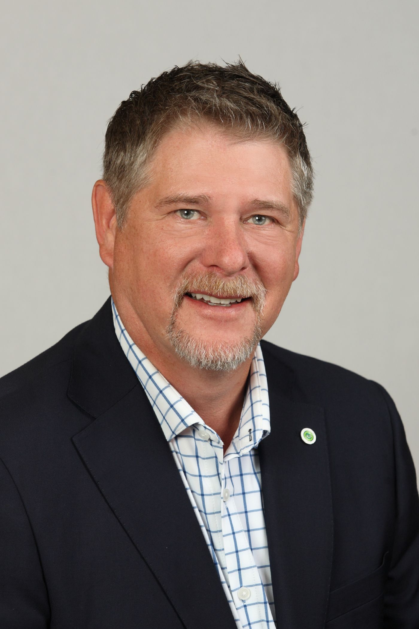 A bald man wearing a green nike jacket is standing in front of a white wall.