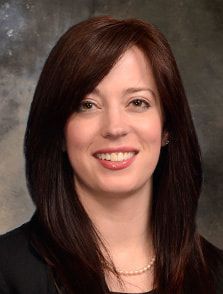 A woman with long brown hair and a pearl necklace is smiling for the camera.