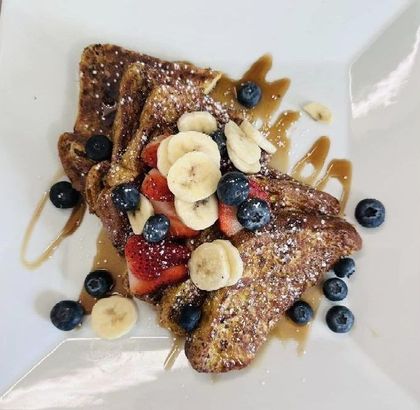 French toast with bananas strawberries and blueberries on a white plate