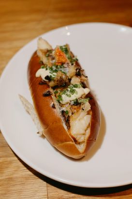 A close up of a hot dog on a white plate on a wooden table.