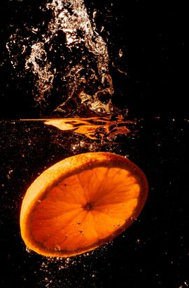 A slice of orange is falling into the water