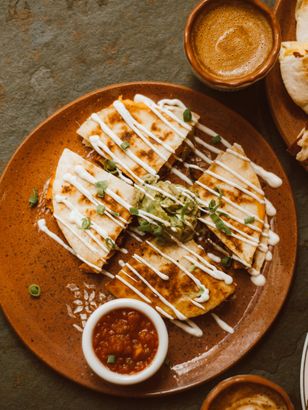 A plate of quesadillas with guacamole and sour cream on a table.