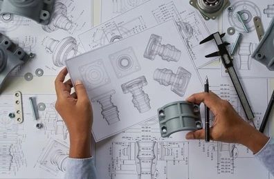 una persona sostiene un trozo de metal y mira un dibujo en una hoja de papel.