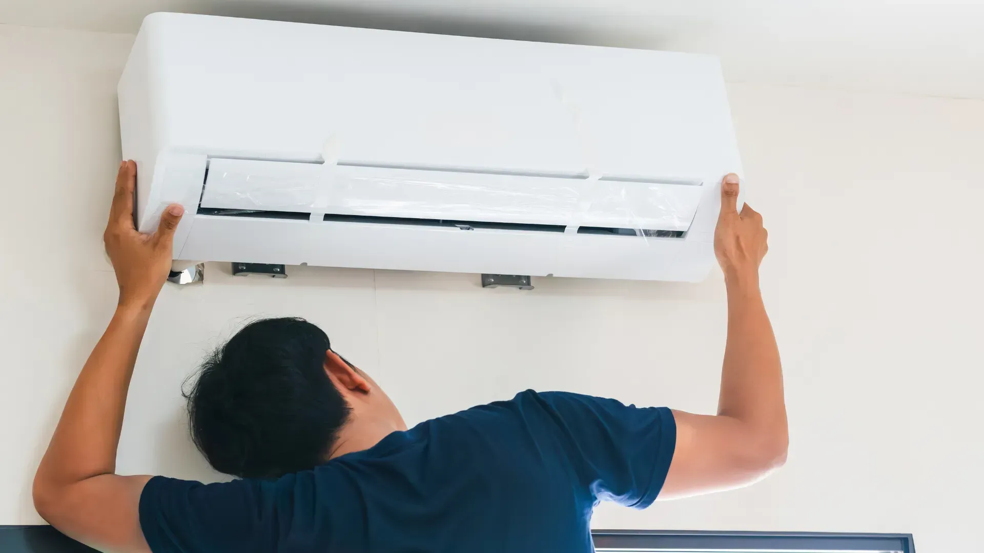 A man is installing an air conditioner on the wall.