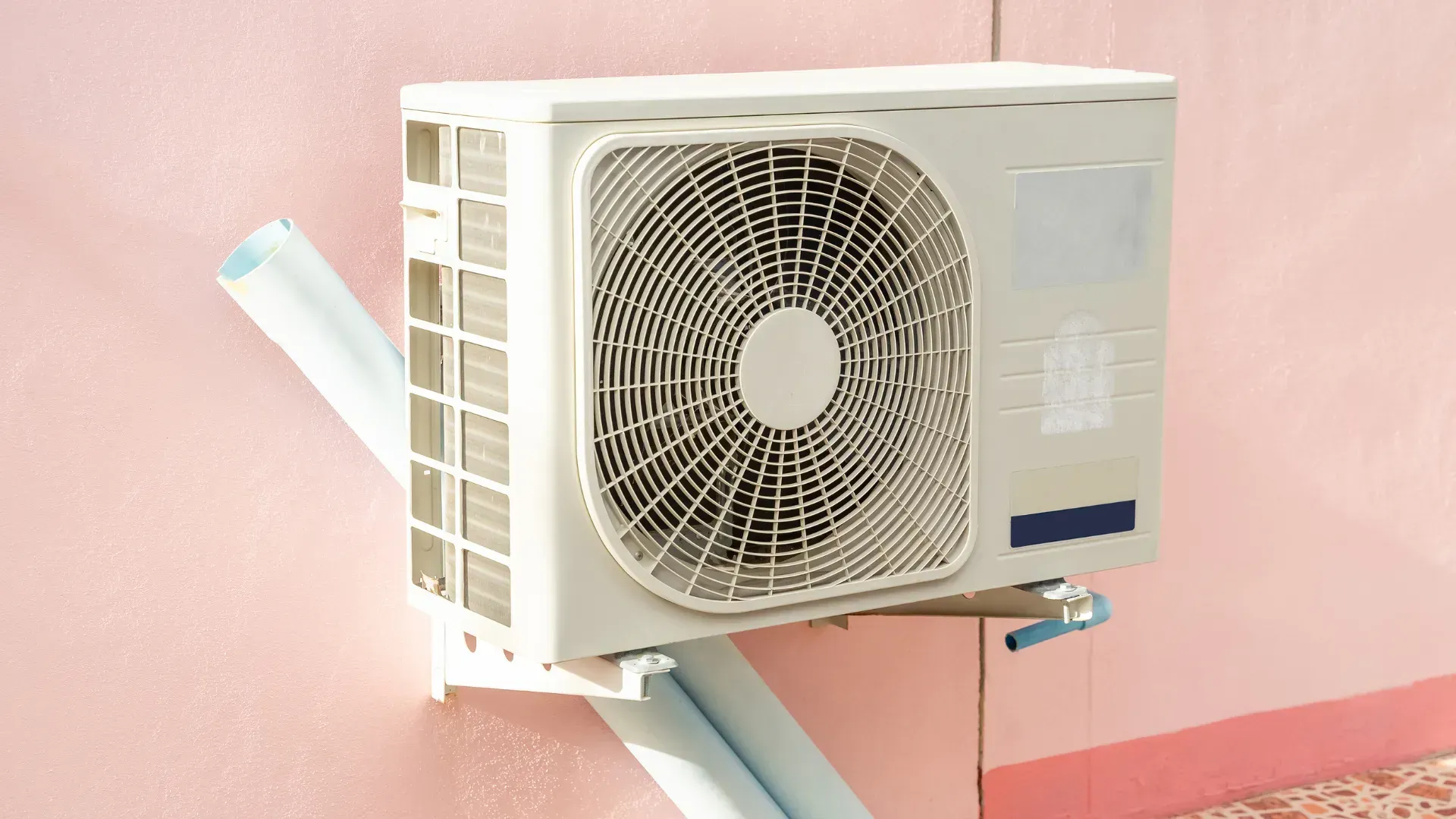 A white air conditioner is mounted on a pink wall.