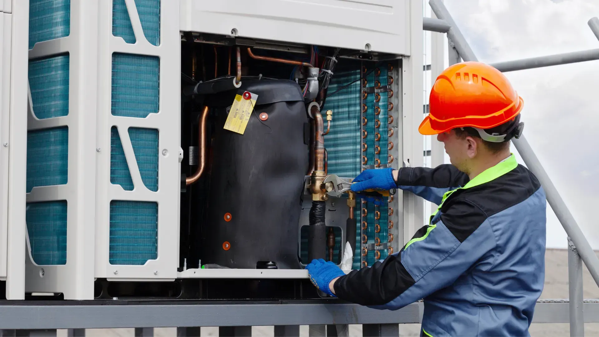 A man wearing a hard hat is working on an air conditioner.