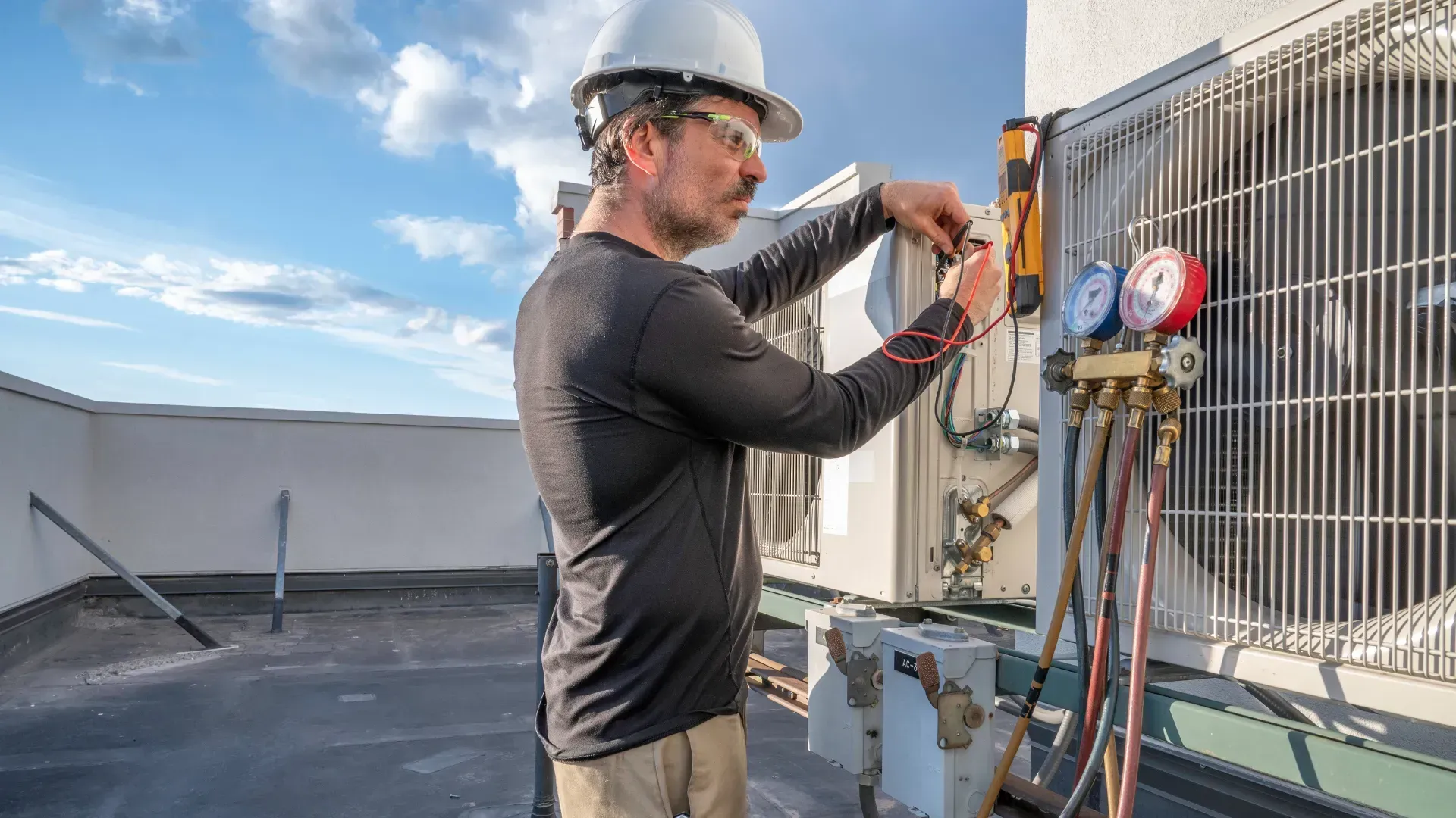 A man is working on an air conditioner on the roof of a building.