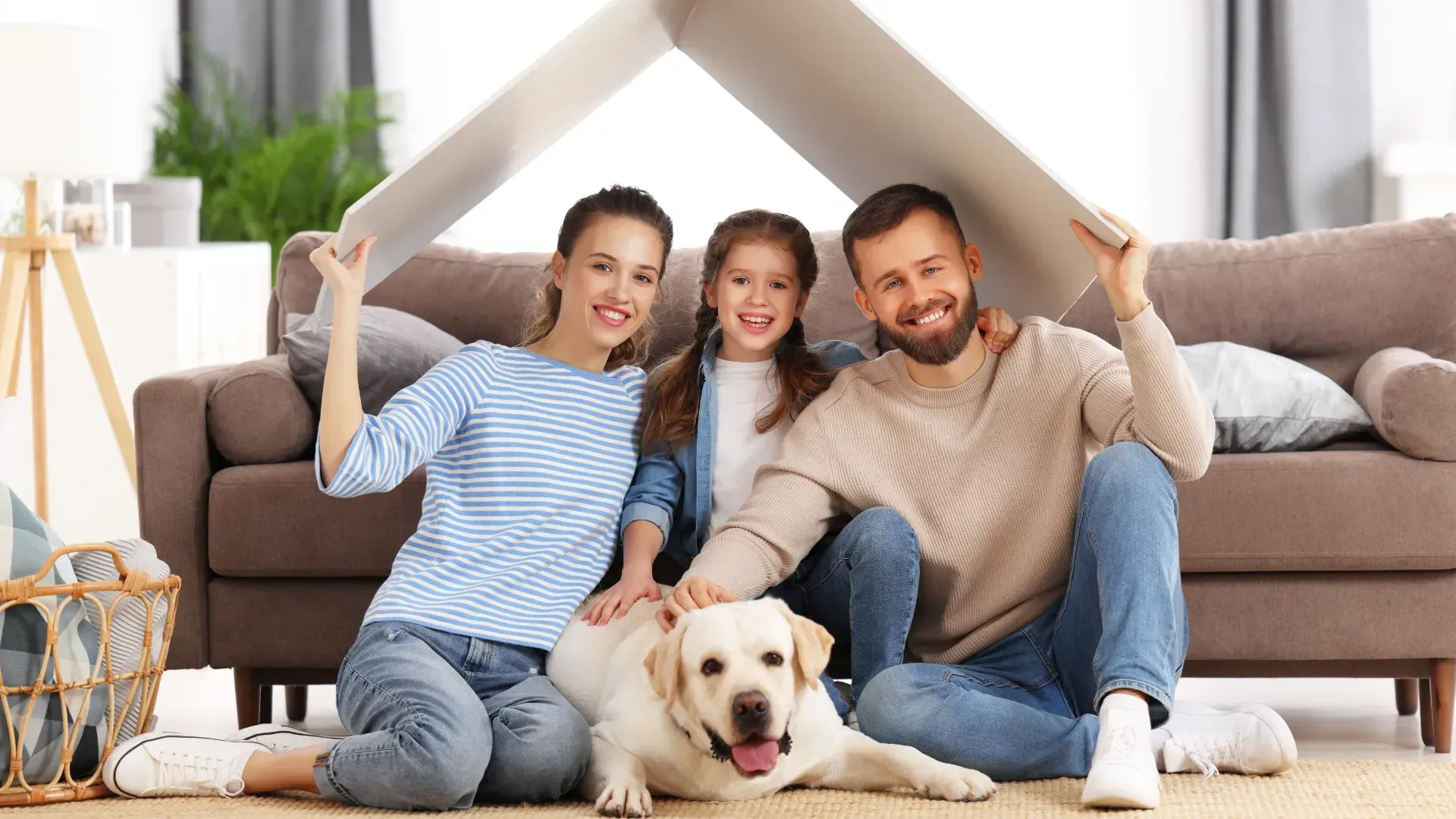 A family is sitting on the floor with a dog under a cardboard house.