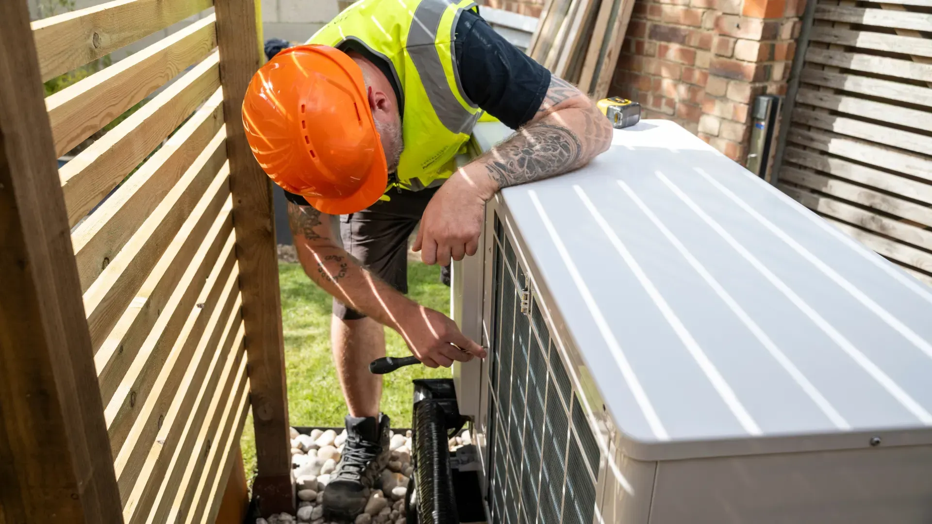 A man wearing a hard hat is working on an air conditioner.