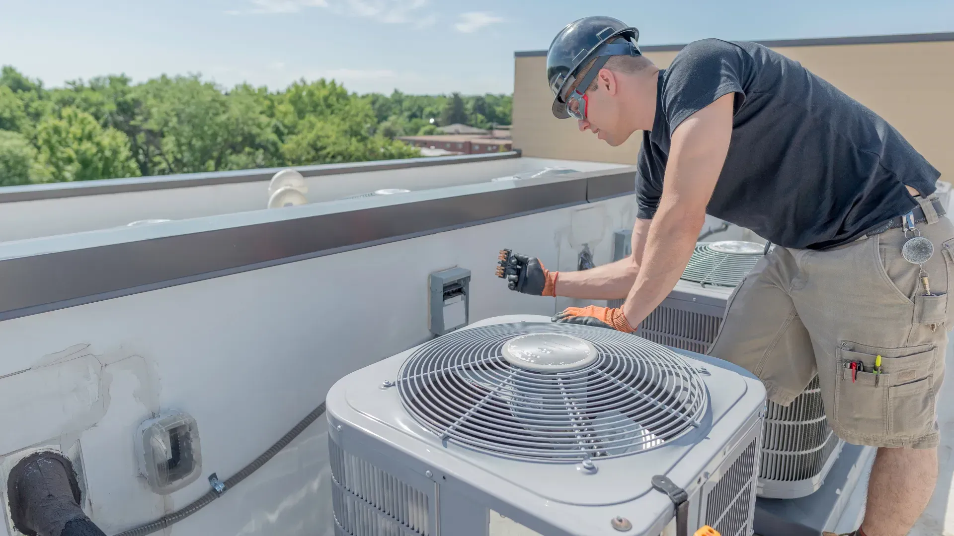 A man is working on an air conditioner on the roof of a building.