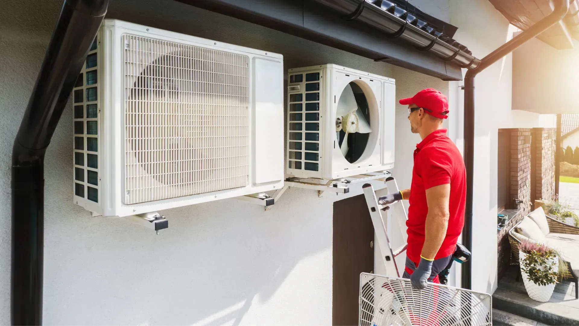 A man is installing an air conditioner on the side of a house.