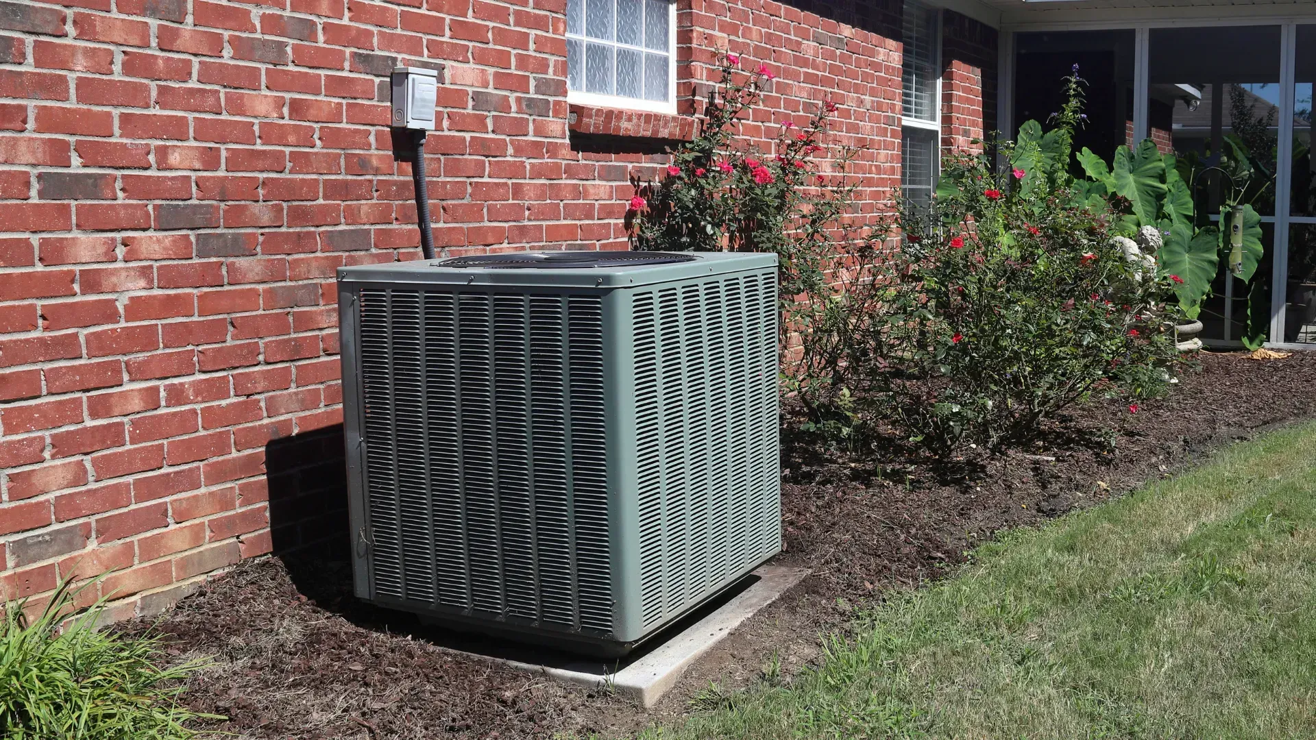 An air conditioner is sitting on the side of a brick house.