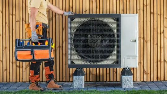 A man is holding a toolbox next to a fan.
