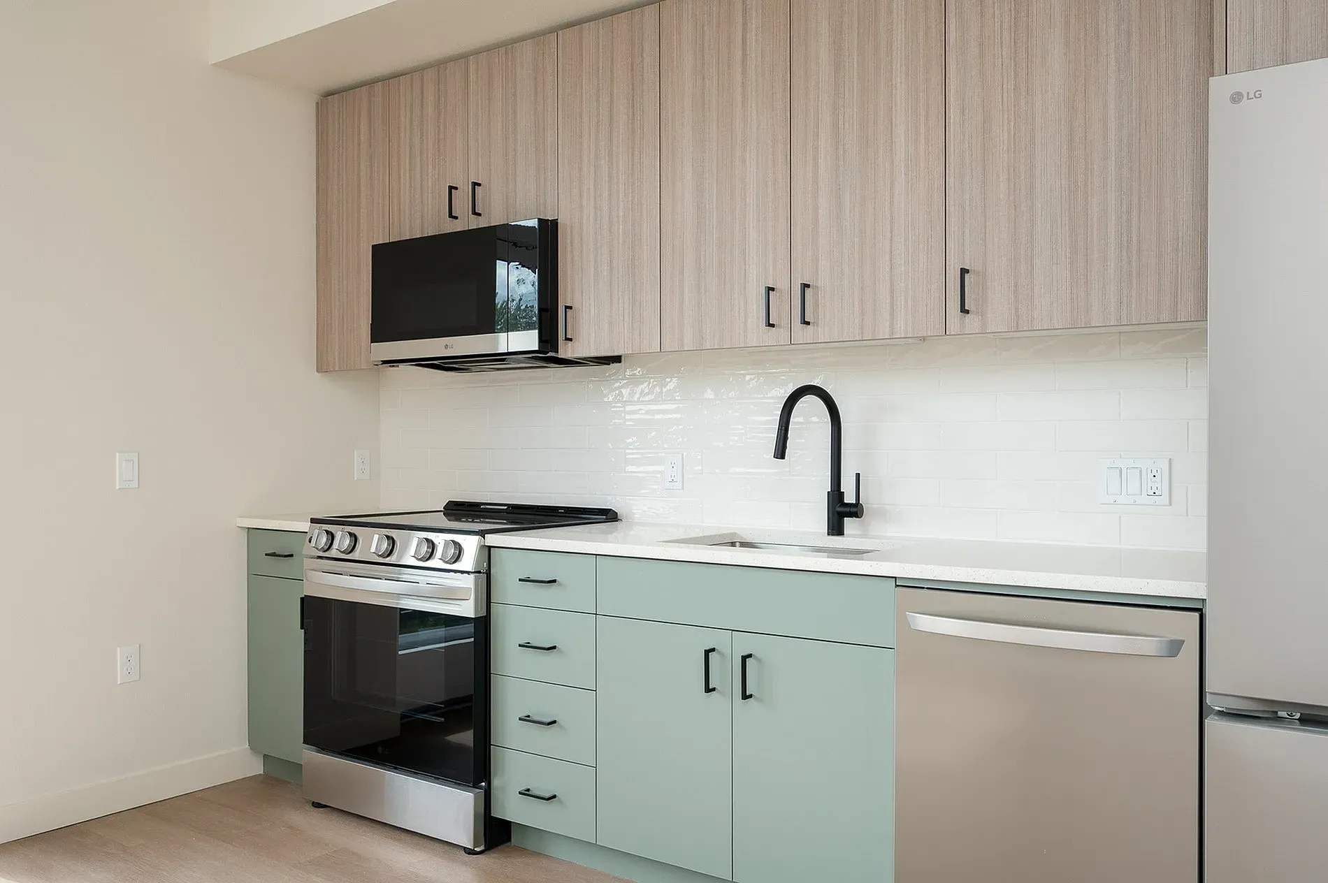 Modern kitchen with light wood cabinets, pale green lower cabinets, stainless steel appliances, and a black faucet.