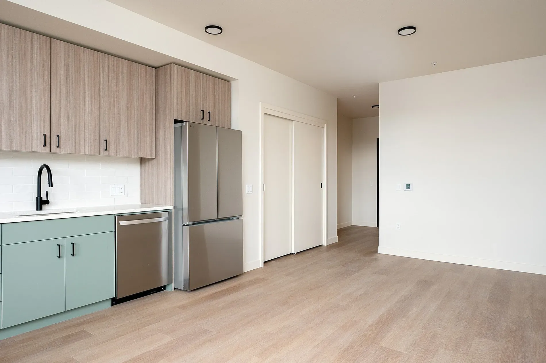 Modern kitchen and living area with light wood floors and stainless steel appliances.