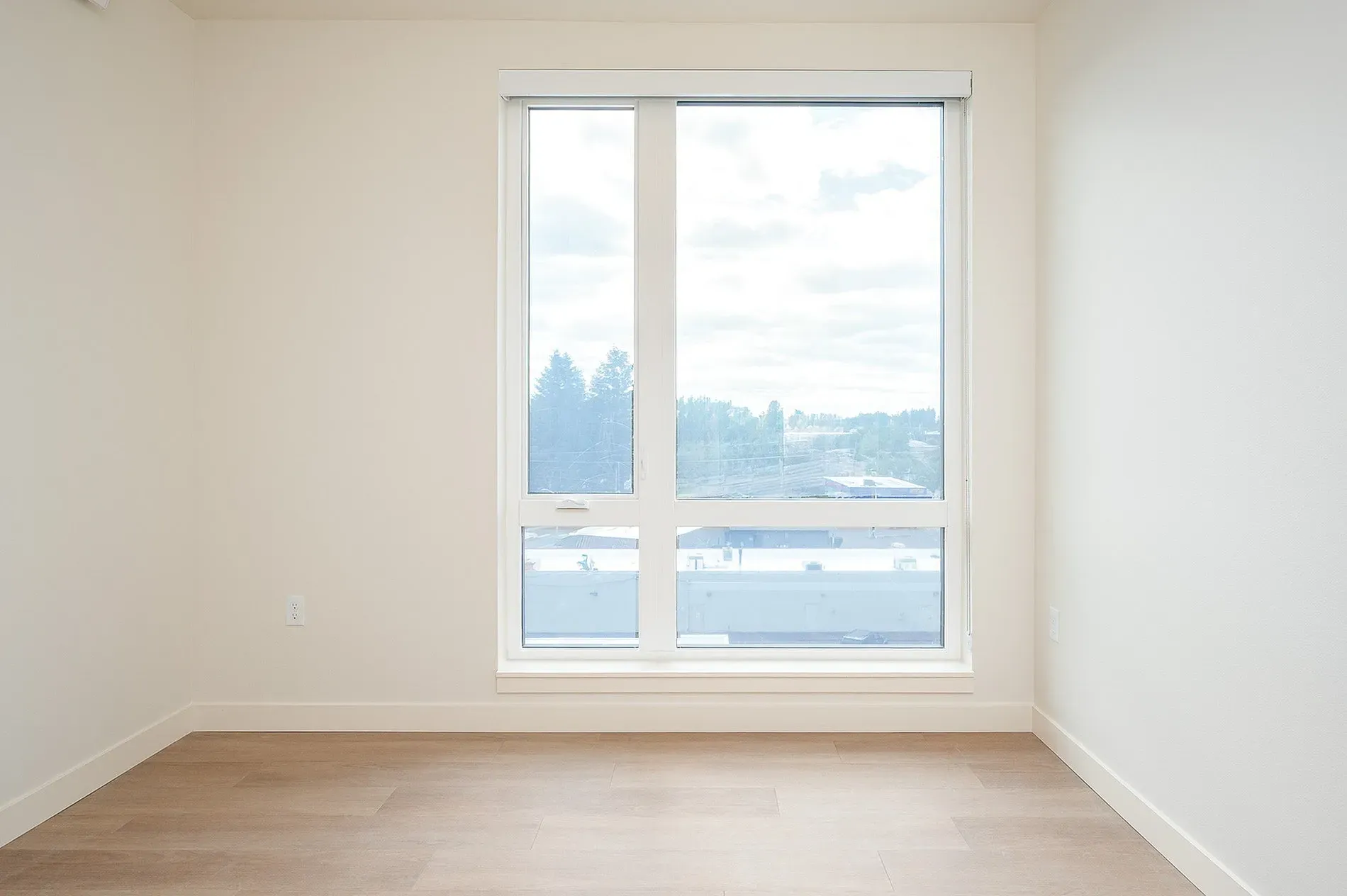 Empty room with large window overlooking trees and buildings