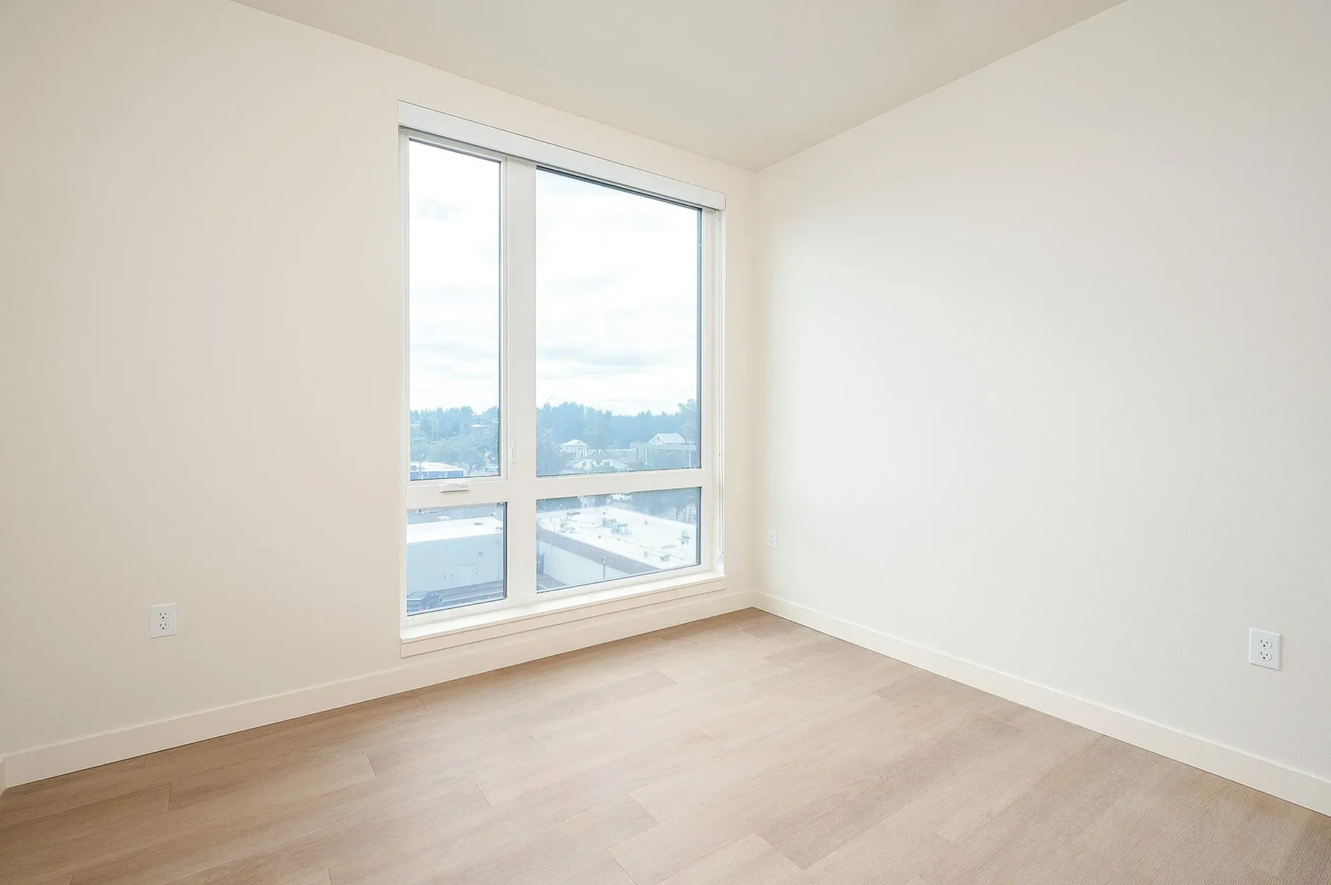 Empty room with large window and light wood floors.