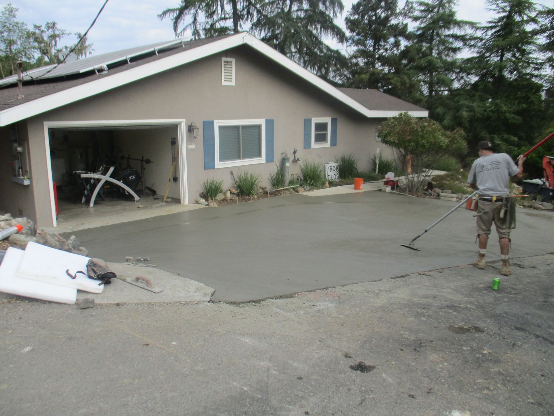 Residential driveway being resurfaced, with wet concrete, an open garage, and a worker on the right.