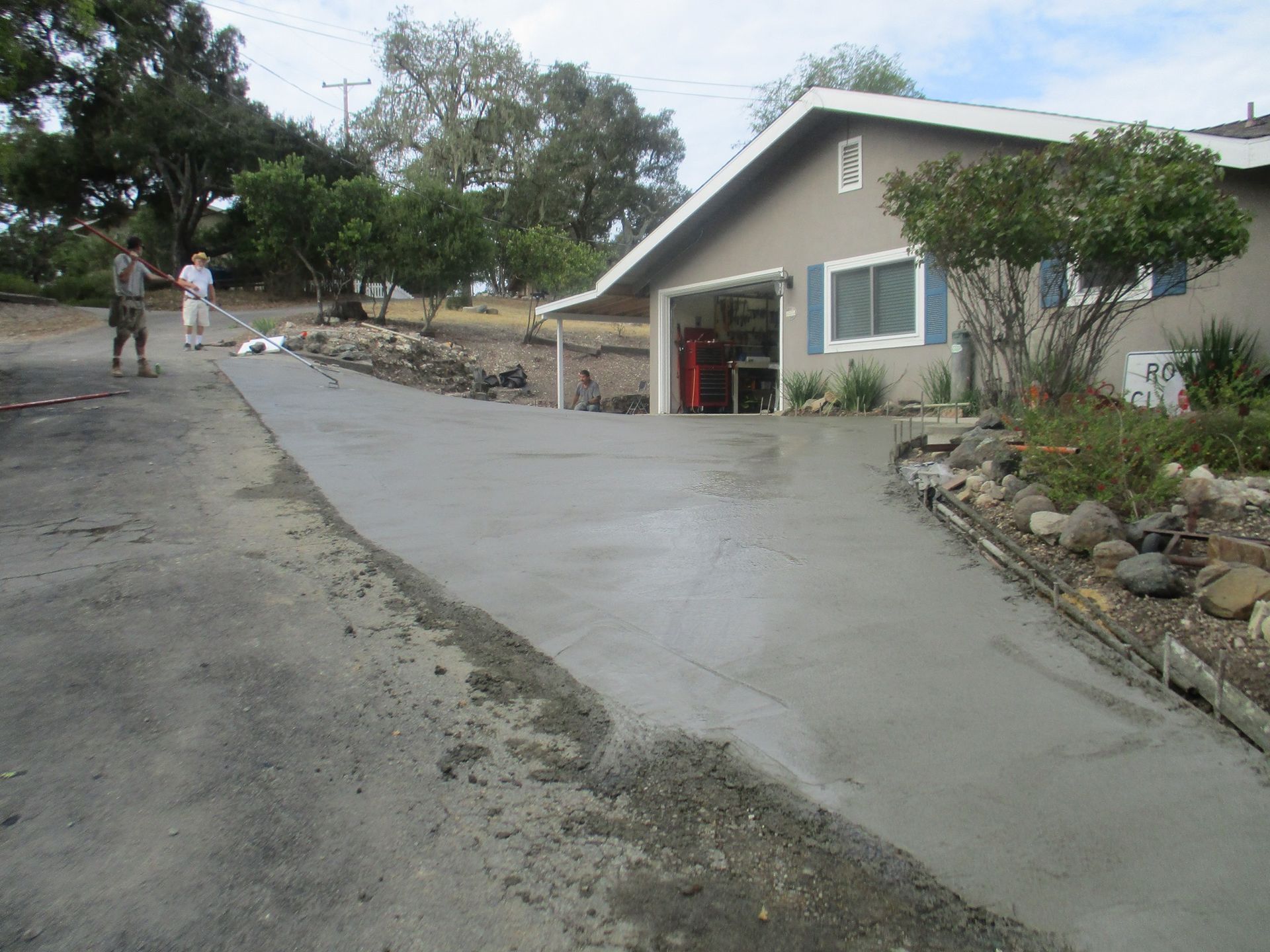 Concrete driveway leading to a gray house with rock landscaping and two people in the distance