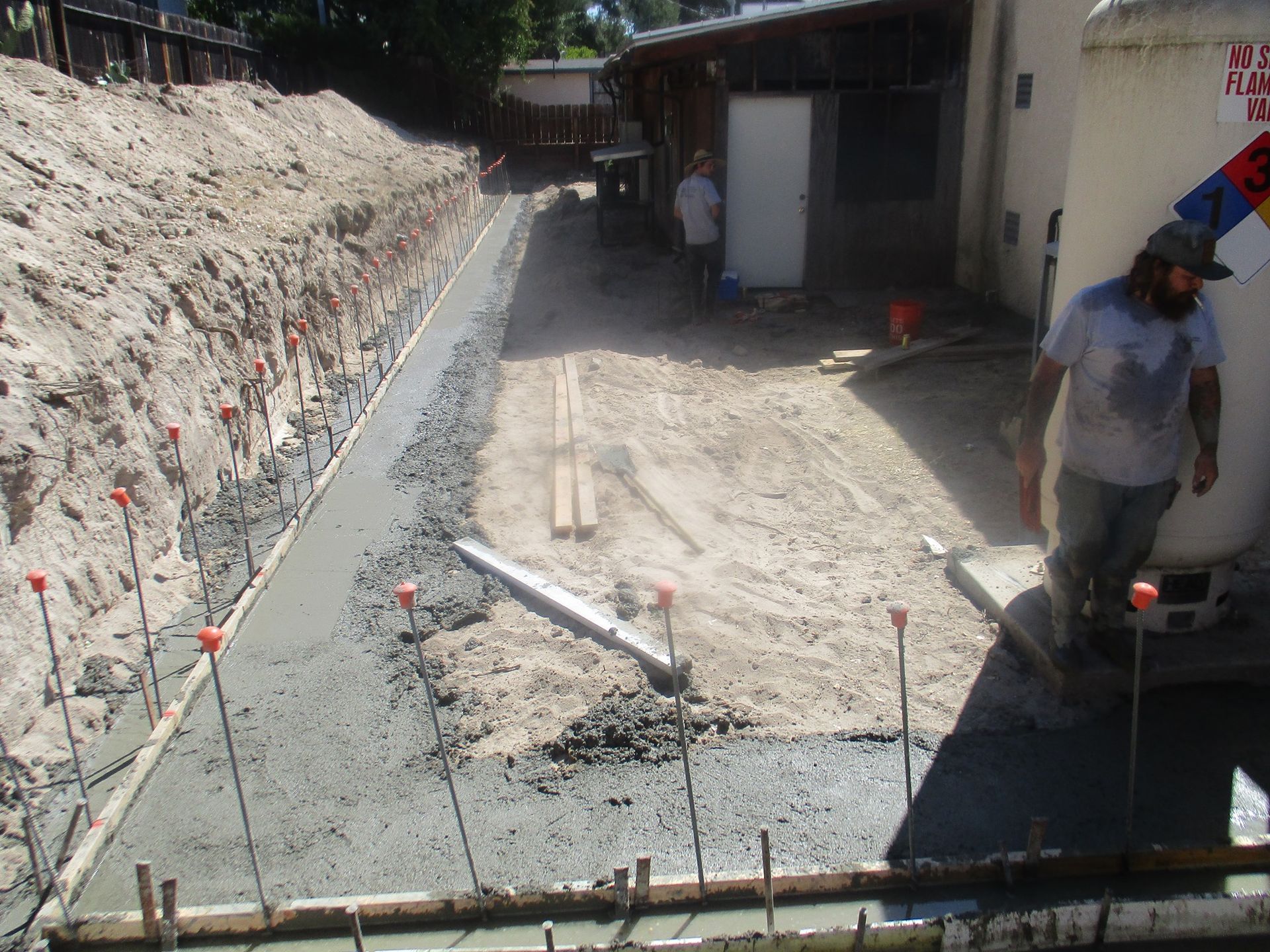 Construction site trench with workers, gravel foundation, and white building wall