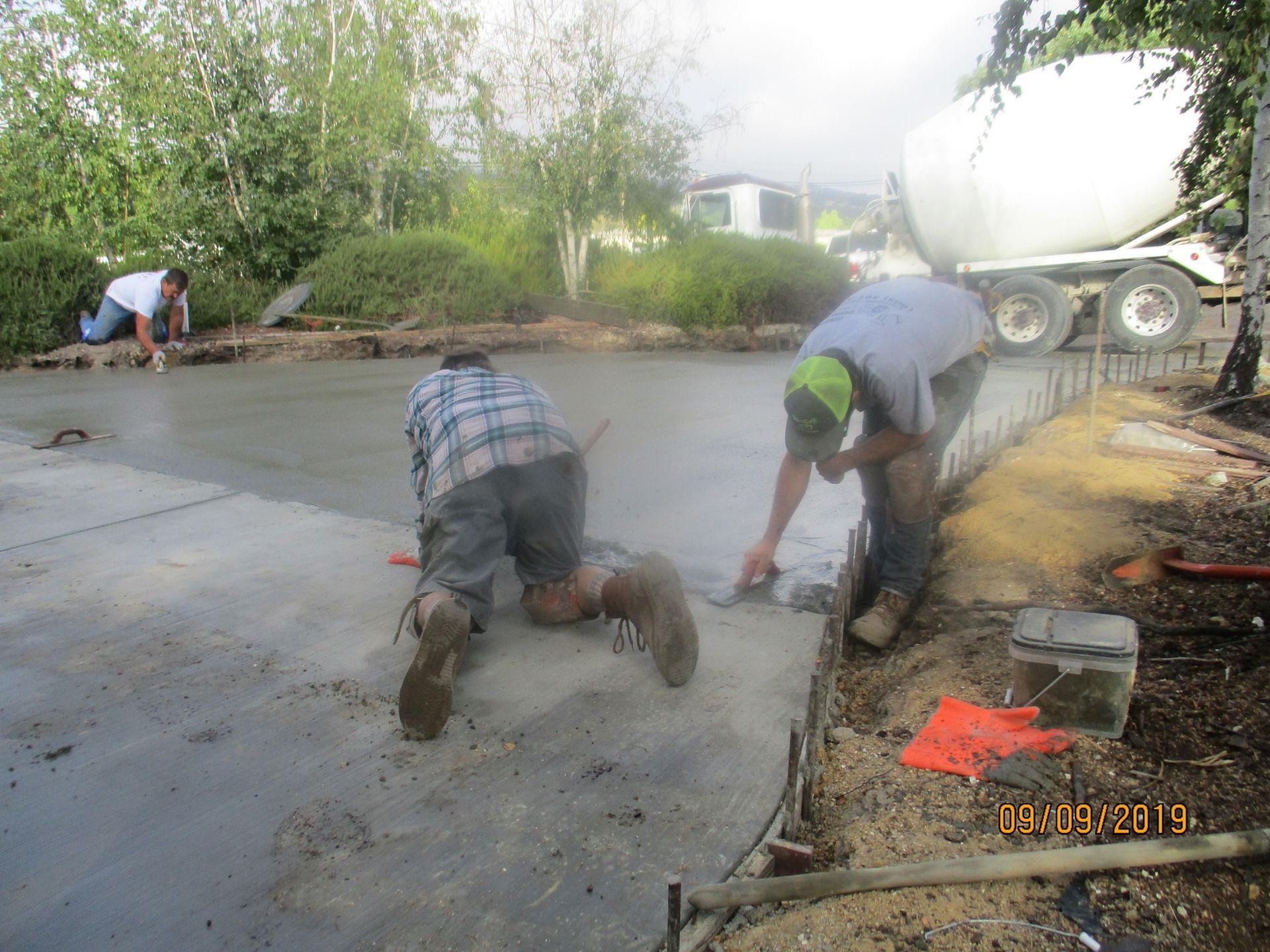 Workers kneeling on a concrete roadway, smoothing wet pavement beside a cement mixer truck.