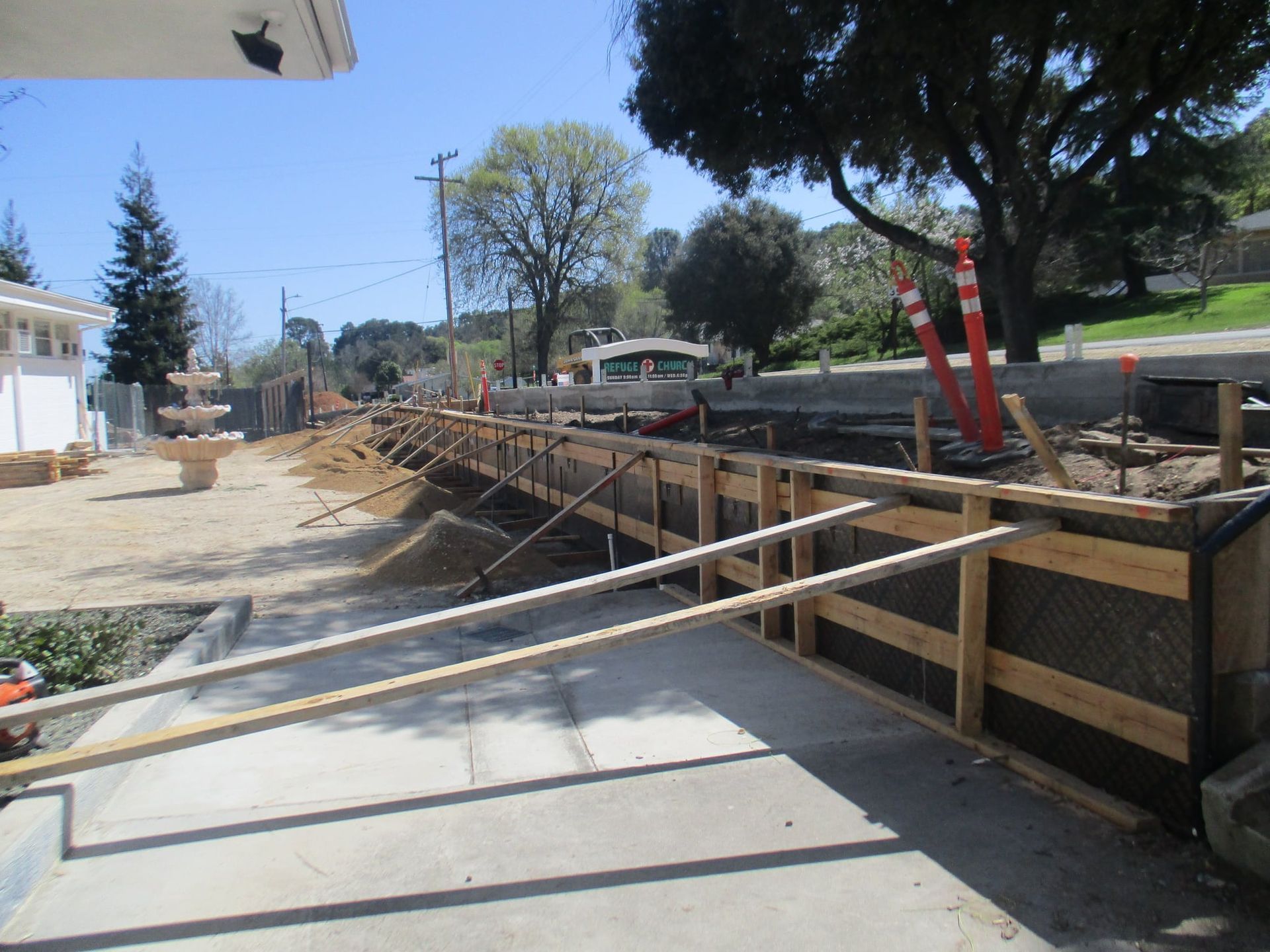 Roadside construction site with wooden retaining wall and diagonal support beams beside a concrete path