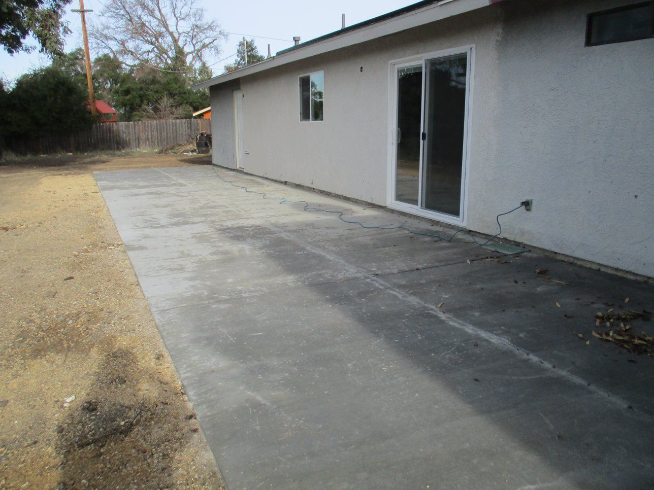 Concrete patio beside a white house with a sliding glass door and gravel yard