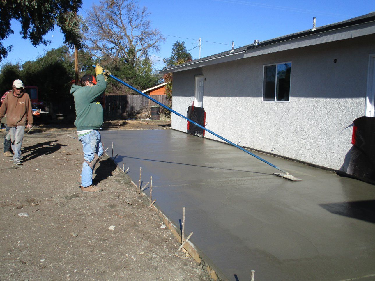 Workers smoothing fresh concrete beside a white house on a sunny day