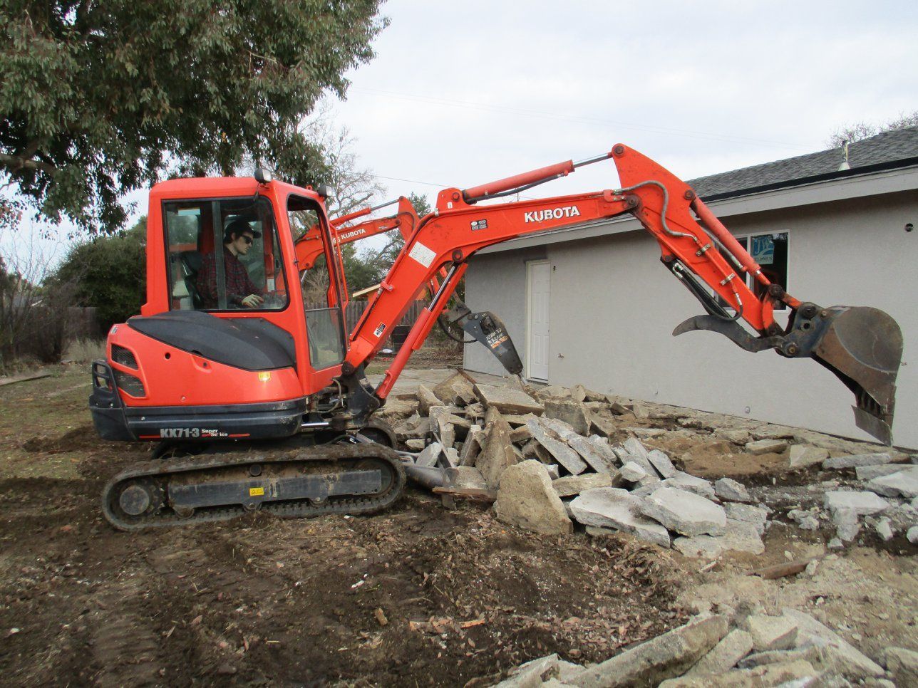 Orange excavator demolishing concrete rubble beside a building