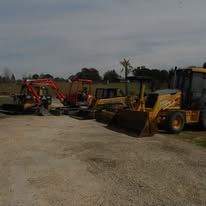 Construction equipment parked on a gravel lot, including a yellow loader and red excavator.