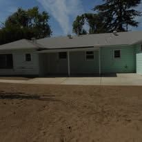 Single-story house with a carport, white siding, and a concrete driveway under a blue sky.