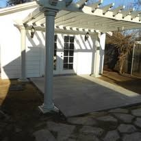 White patio with pergola, column, and stone paving outside a house